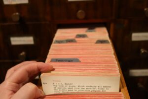 Una mano sfoglia le schede di un archivio cartaceo a cassetti.